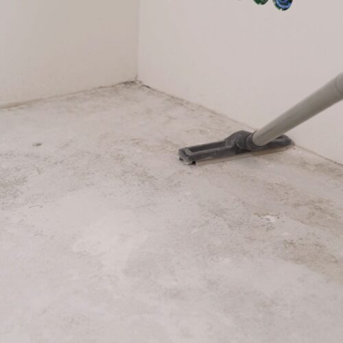 A worker removes dust with a vacuum cleaner. A worker with an industrial vacuum cleaner removes dust from repairs. Floor preparation for renovation. Cleaning cement floor with vacuum cleaner